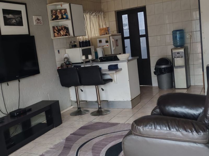 Open plan living area featuring a breakfast bar, tiled flooring, and a functional kitchen space with built-in cabinetry and tiled splashbacks.