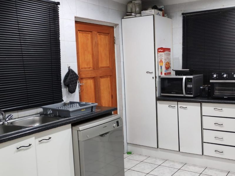 A functional kitchen featuring white cabinetry, laminate countertops, tiled flooring, and built-in appliances, offering a practical layout with potential for modern updates.