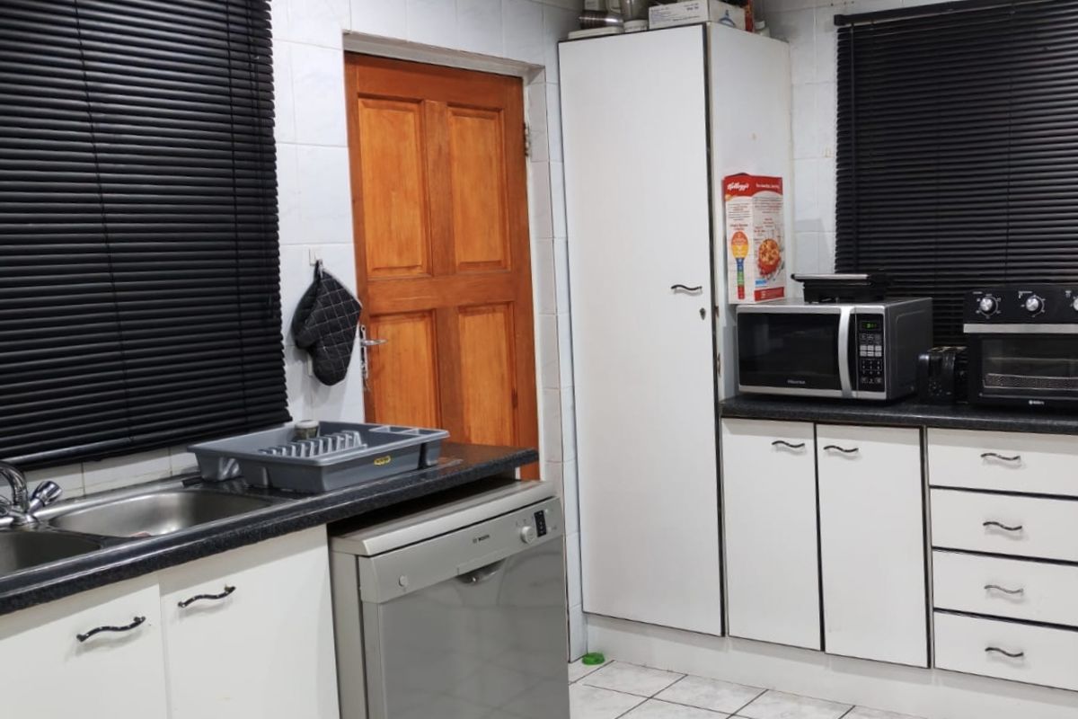 A functional kitchen featuring white cabinetry, laminate countertops, tiled flooring, and built-in appliances, offering a practical layout with potential for modern updates.