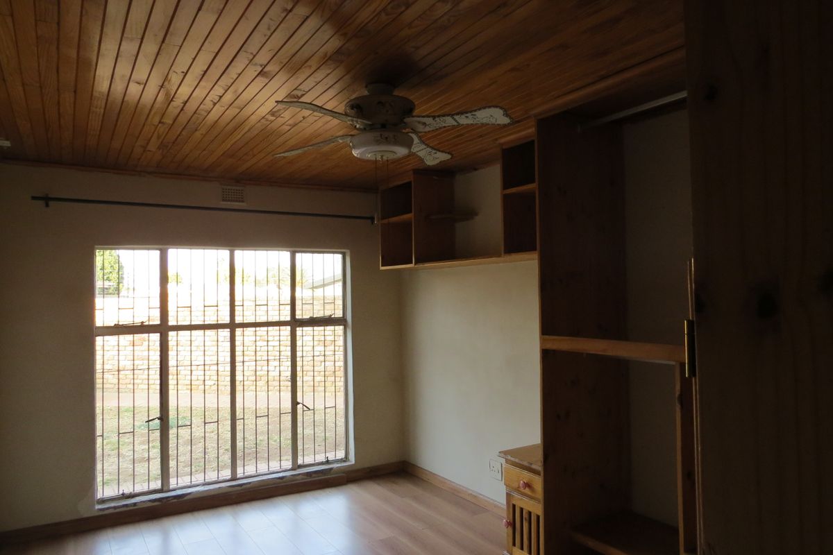 A bedroom featuring a timber-clad ceiling, ceiling fan, built-in wooden cupboards, laminate flooring, and security bars on the window.