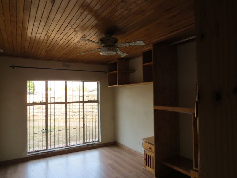 A bedroom featuring a timber-clad ceiling, ceiling fan, built-in wooden cupboards, laminate flooring, and security bars on the window.