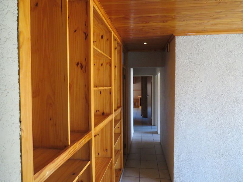 A hallway featuring built-in wooden shelving, a timber-clad ceiling, and tiled flooring, leading towards other areas of the home.