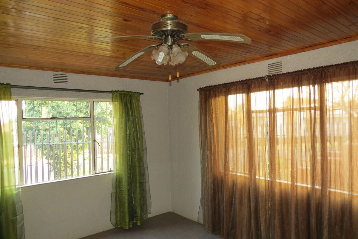 A bright living area featuring a timber tongue and groove ceiling, ceiling fan, and large windows with security bars.
