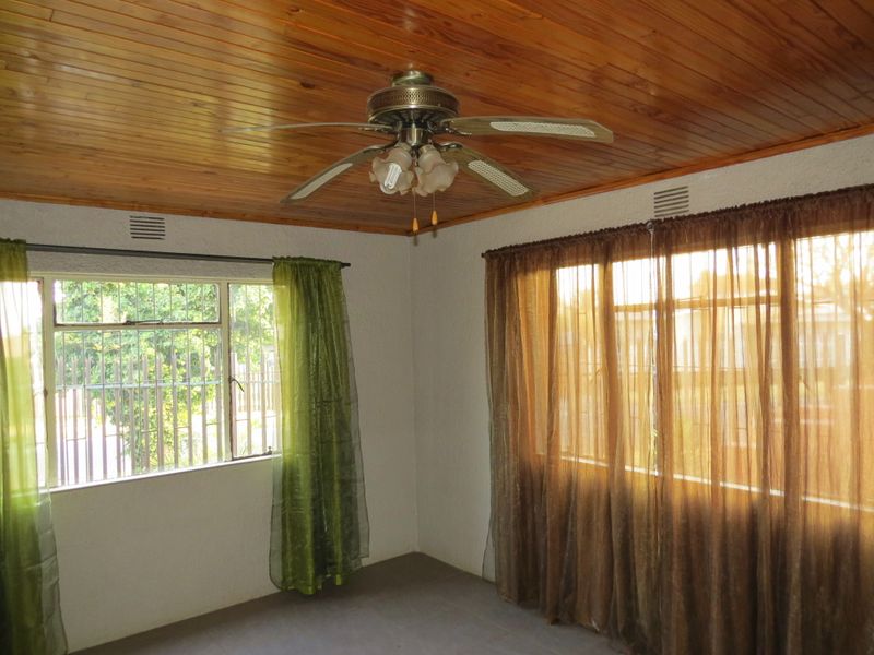 A bright living area featuring a timber tongue and groove ceiling, ceiling fan, and large windows with security bars.