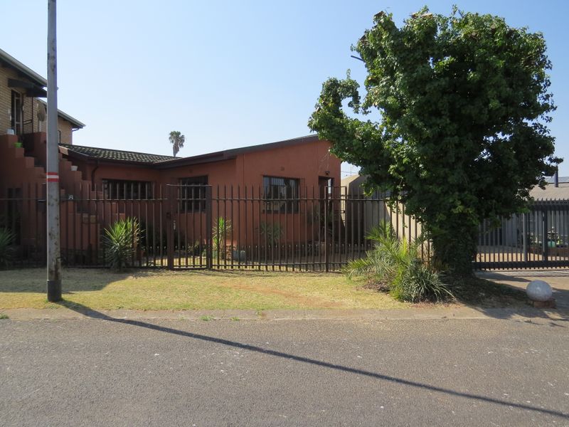Front exterior view of a single-story house featuring a metal security fence, security bars on windows, and a paved driveway.