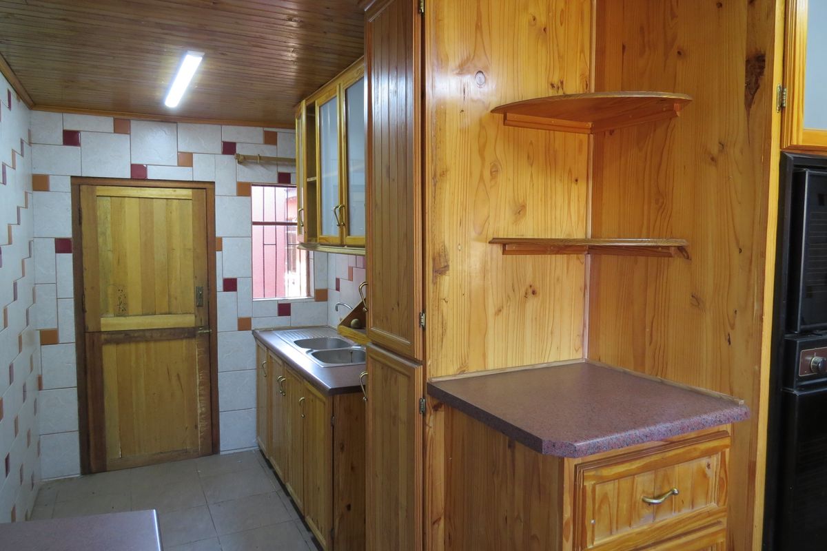 A dated kitchen featuring extensive timber cabinetry, laminate countertops, a double bowl sink, and a timber-paneled ceiling with fluorescent lighting.