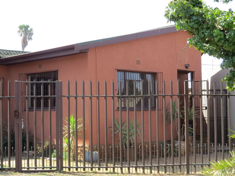 Front elevation of a single-story house featuring terracotta-colored exterior walls, security fencing, and protective window bars.