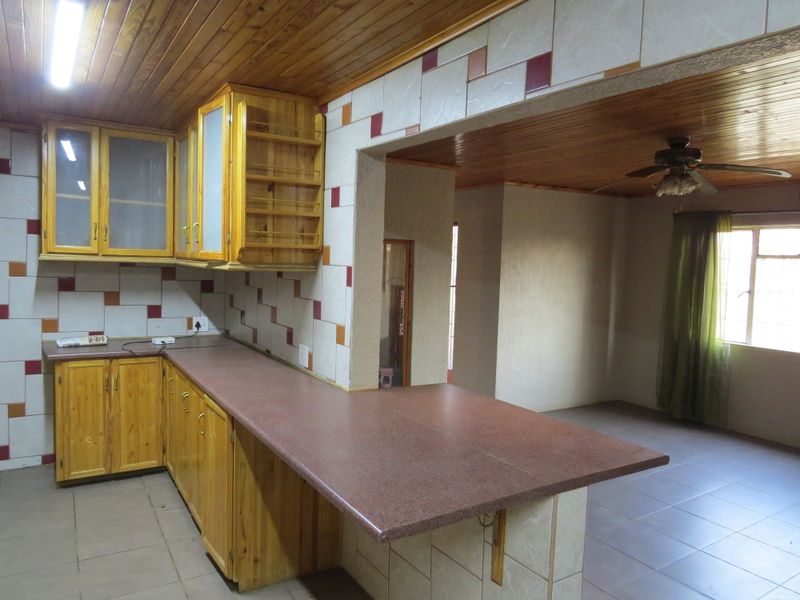 Open plan kitchen and living area featuring timber ceilings, tiled flooring, and wooden cabinetry with a breakfast bar counter.
