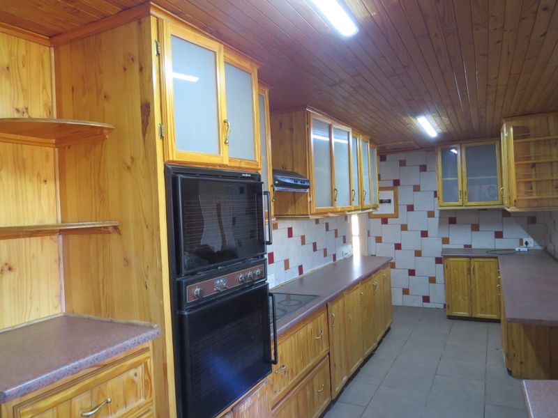 A functional kitchen featuring extensive built-in wooden cabinetry, integrated oven and hob, tiled splashbacks, and a timber-clad ceiling.