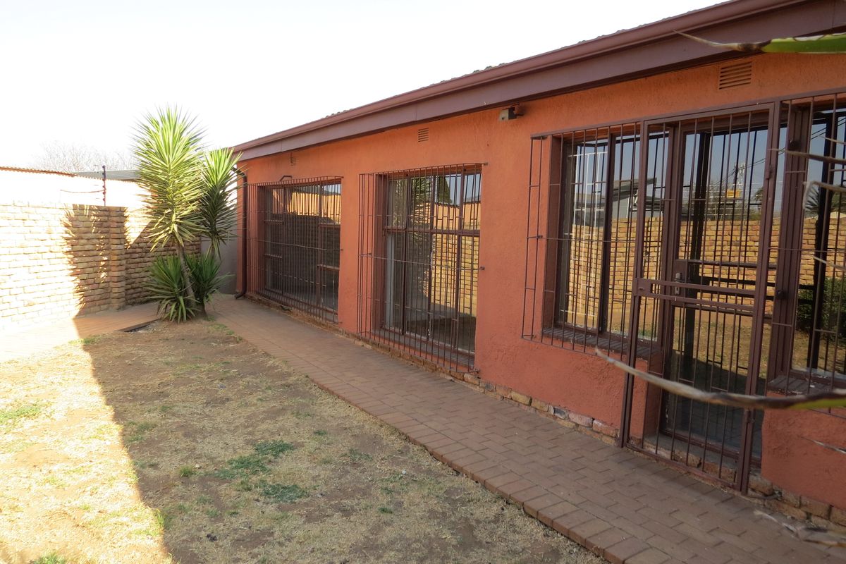 Rear exterior view of the house featuring a paved walkway, security bars on windows, and a brick boundary wall.