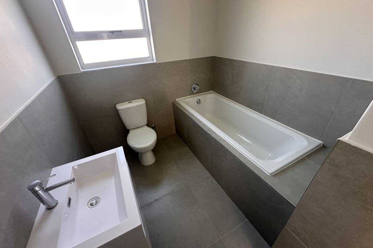 A modern bathroom featuring a built-in bathtub, a contemporary vanity basin, and a toilet, finished with neutral grey floor and wall tiling.