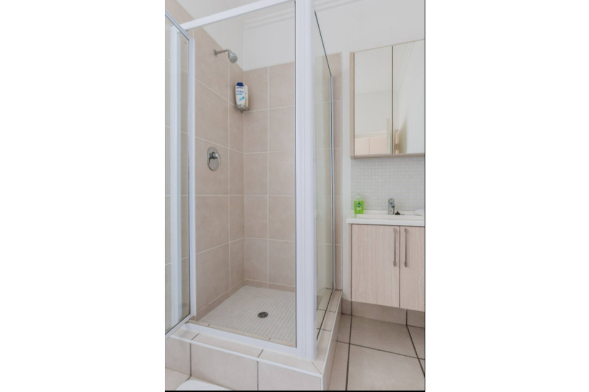 A clean, functional bathroom featuring a glass-enclosed shower with tiled walls and a wall-mounted vanity cabinet with an integrated mirror.