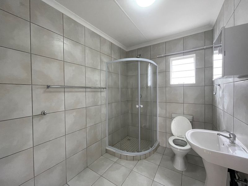 A functional bathroom featuring a corner shower enclosure, pedestal basin, and toilet, finished with neutral wall and floor tiling.