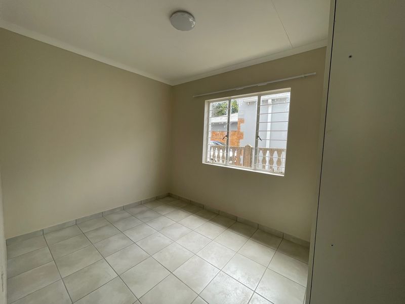 A clean, empty bedroom featuring neutral wall paint, tiled flooring, and a window fitted with security bars.