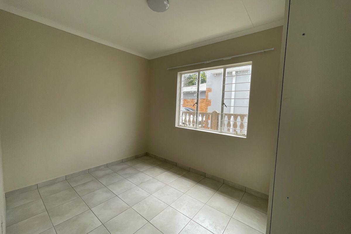 A clean, empty bedroom featuring neutral wall paint, tiled flooring, and a window fitted with security bars.