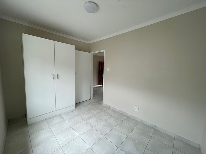 A clean, empty bedroom featuring neutral wall paint, tiled flooring, and a built-in white wardrobe, offering a blank canvas for personalization.