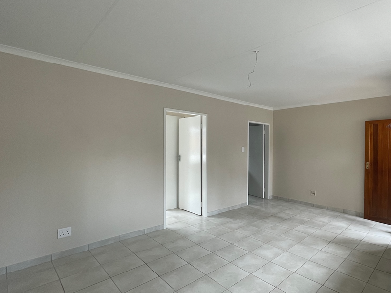 A bright, empty living area featuring neutral wall tones, tiled flooring, and a wooden door, ready for personalization.