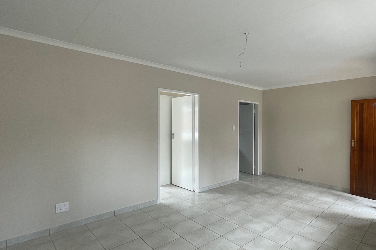 A bright, empty living area featuring neutral wall tones, tiled flooring, and a wooden door, ready for personalization.