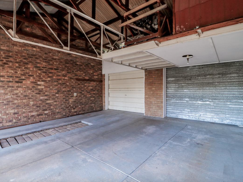 A spacious garage featuring exposed brick walls, timber roof trusses, a metal roller shutter door, and a built-in inspection pit in the concrete floor.