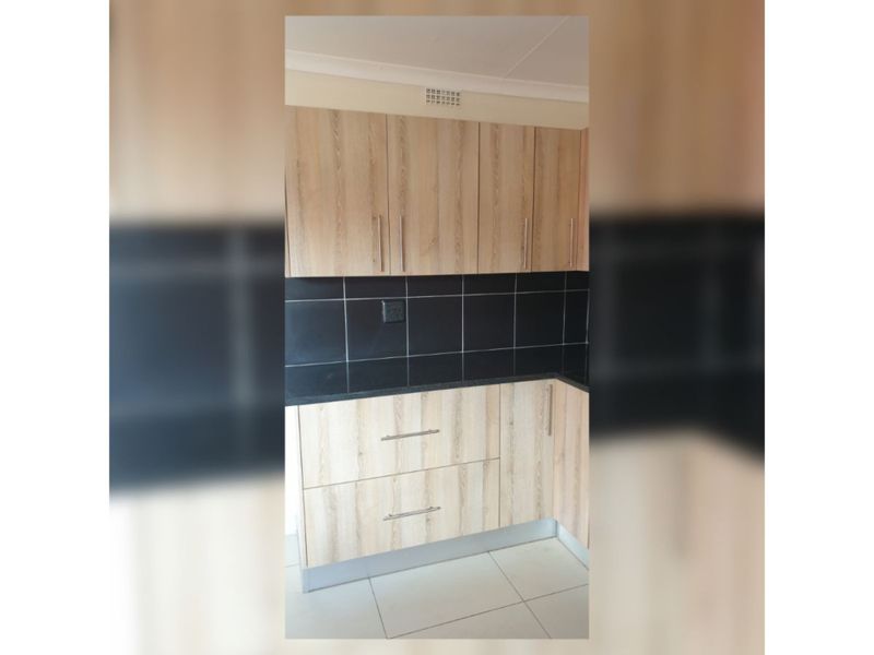 A clean kitchen corner featuring light wood-grain cabinetry, contrasting black granite countertops, and a black tiled backsplash with neutral floor tiles.