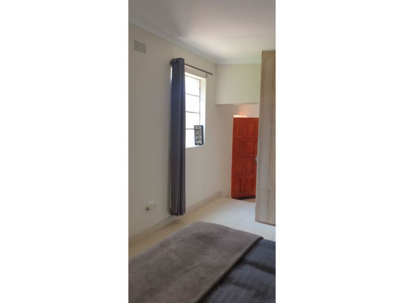 A bedroom featuring tiled flooring, a built-in wardrobe, and a timber door, providing a functional and neutral living space.
