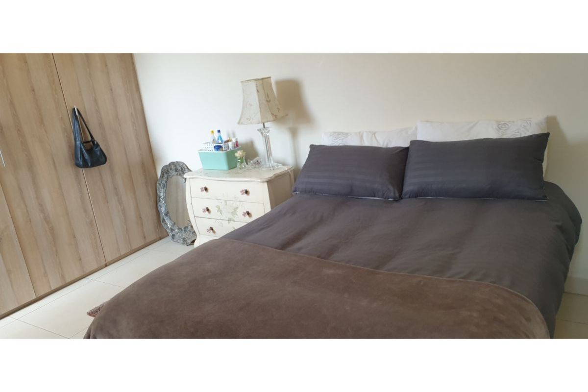 A functional bedroom featuring light-toned tiled flooring and a built-in wardrobe with wood-grain finish doors.