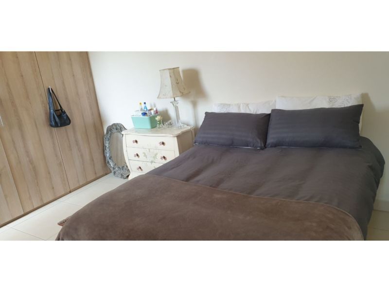 A functional bedroom featuring light-toned tiled flooring and a built-in wardrobe with wood-grain finish doors.