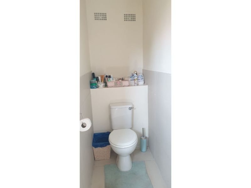 A compact bathroom featuring a standard toilet, tiled flooring, and half-tiled walls with integrated ventilation grilles.