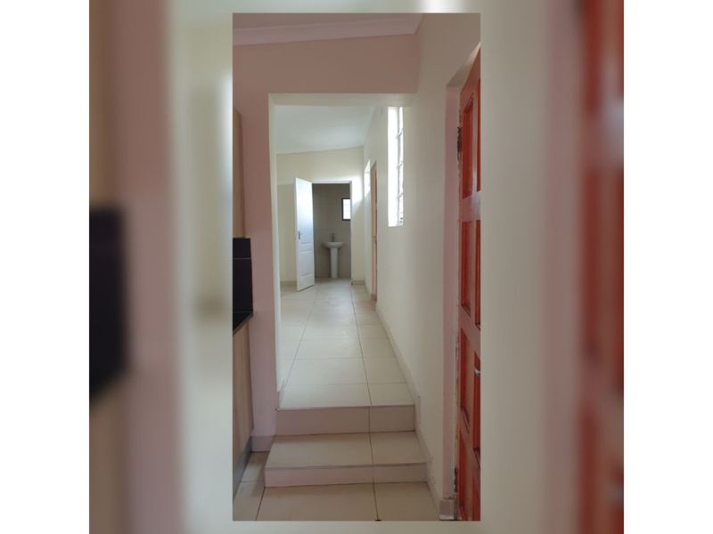 A tiled hallway featuring a stepped transition and a pedestal basin visible in the adjacent room, providing a clean and functional layout.