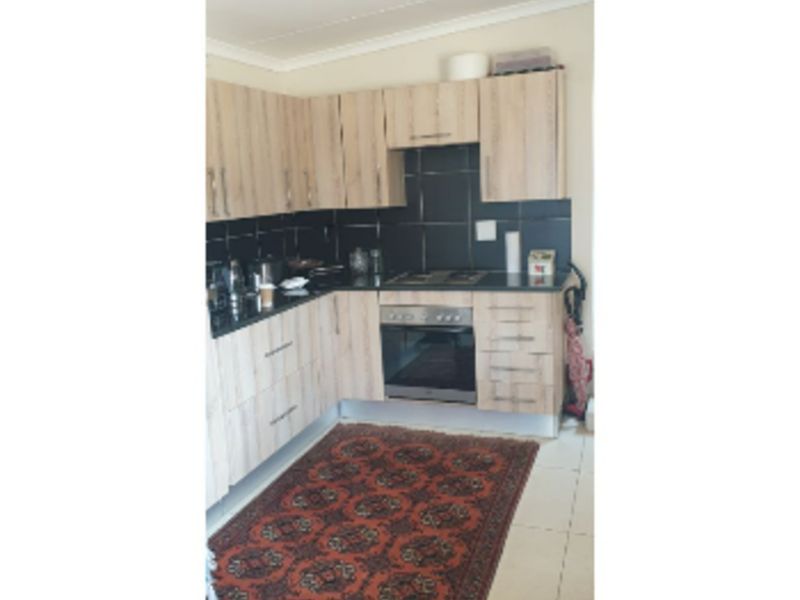 A functional kitchen featuring light wood-tone cabinetry, dark tiled backsplash, built-in oven, and cooktop with neutral floor tiles.