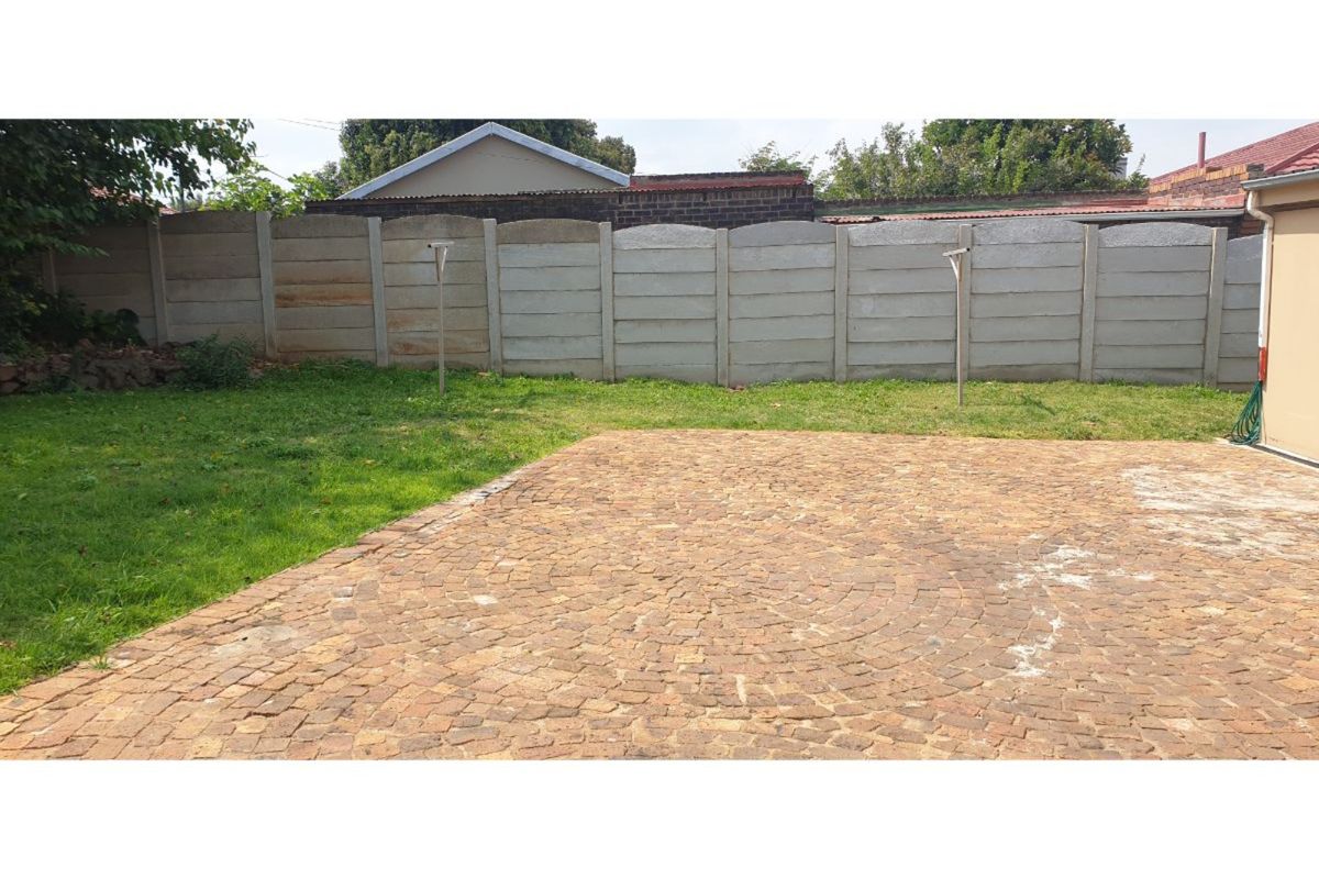 A rear garden area featuring a brick-paved patio, a lawn, and a precast concrete boundary wall.