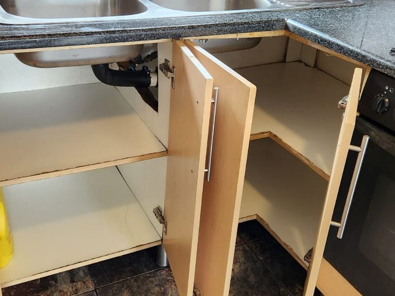 A close-up view of a kitchen base cabinet unit featuring a double sink, granite countertop, and integrated oven with visible wear on cabinetry.