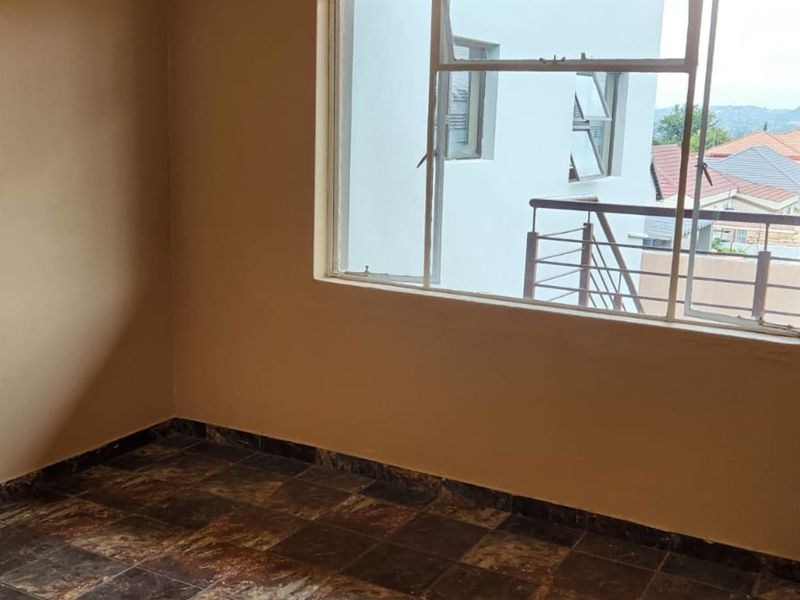 An empty bedroom featuring tiled flooring, a built-in cupboard, and a large window with views of the surrounding neighborhood.