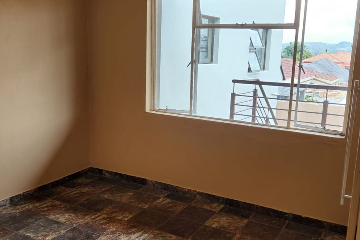 An empty bedroom featuring tiled flooring, a built-in cupboard, and a large window with views of the surrounding neighborhood.