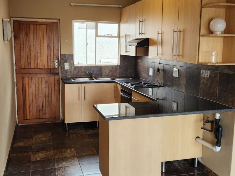 A functional kitchen featuring laminate cabinetry, granite countertops, a built-in hob with extractor, and tiled finishes throughout.