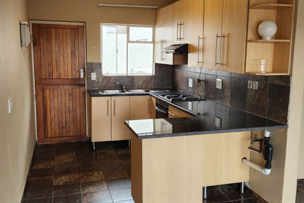 A functional kitchen featuring laminate cabinetry, granite countertops, a built-in hob with extractor, and tiled finishes throughout.