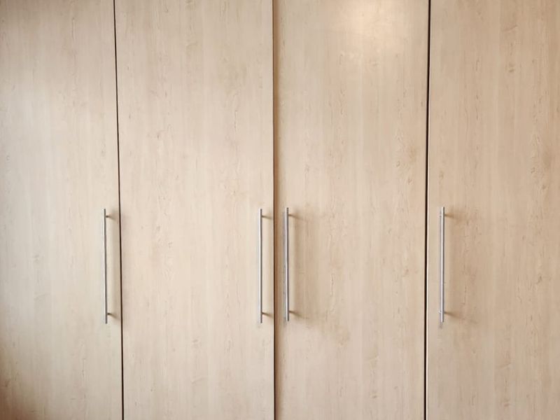 A bedroom featuring light wood-finish built-in wardrobes with modern silver handles.