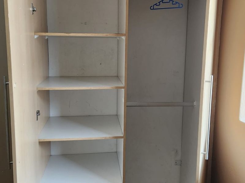 A bedroom featuring a built-in wardrobe with internal shelving and a hanging rail, showing signs of wear and tear.
