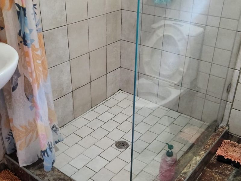 A functional bathroom featuring a glass-enclosed shower, pedestal basin, and toilet, with tiled walls and flooring throughout.