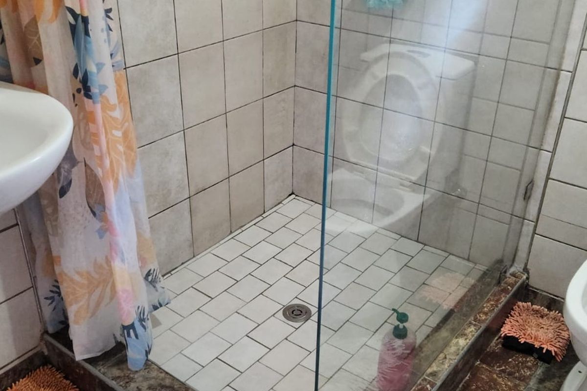 A functional bathroom featuring a glass-enclosed shower, pedestal basin, and toilet, with tiled walls and flooring throughout.