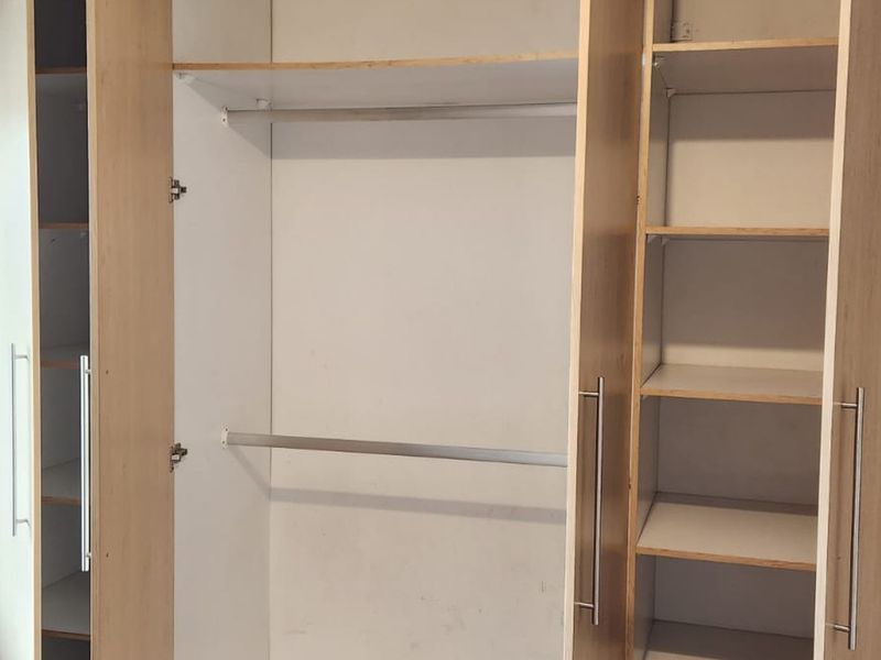 A bedroom featuring a large, light-wood finish built-in wardrobe with integrated shelving and hanging rails.