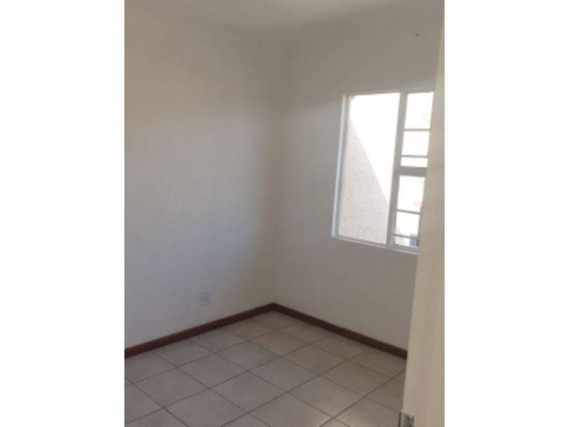 A simple, empty bedroom featuring neutral tiled flooring and a window, providing a blank canvas for personalization.