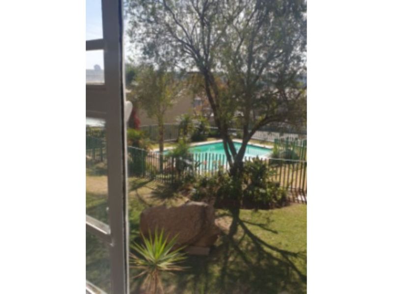 View of a private swimming pool and landscaped garden area, enclosed by metal perimeter fencing, captured from an elevated position.