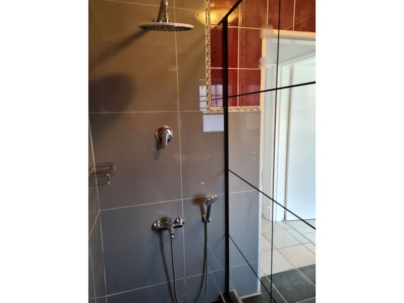 A modern shower enclosure featuring a rain shower head, handheld attachment, and sleek glass screen with grey wall tiling.