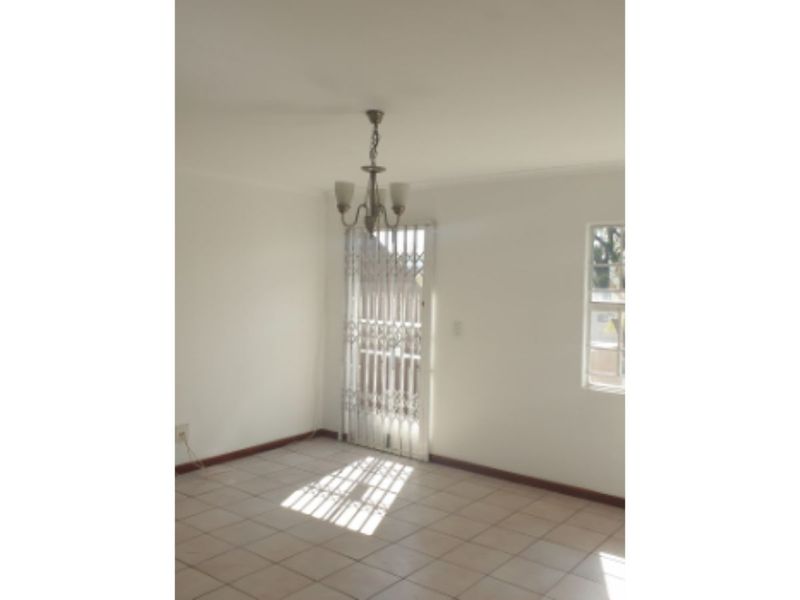An empty living area featuring neutral tiled flooring, a central chandelier, and a security gate leading to the exterior.