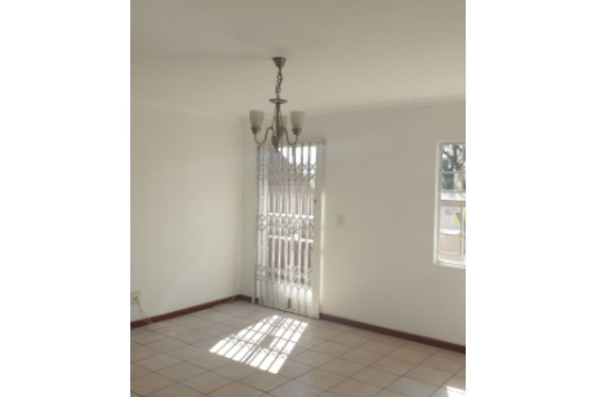 An empty living area featuring neutral tiled flooring, a central chandelier, and a security gate leading to the exterior.