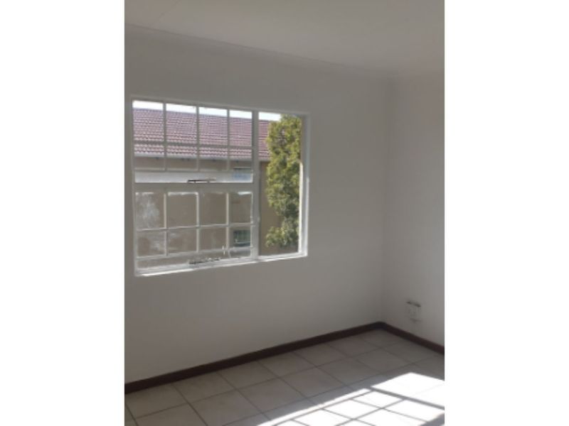 A bright, empty bedroom featuring neutral tiled flooring, white walls, and a grid-pattern window providing natural light.