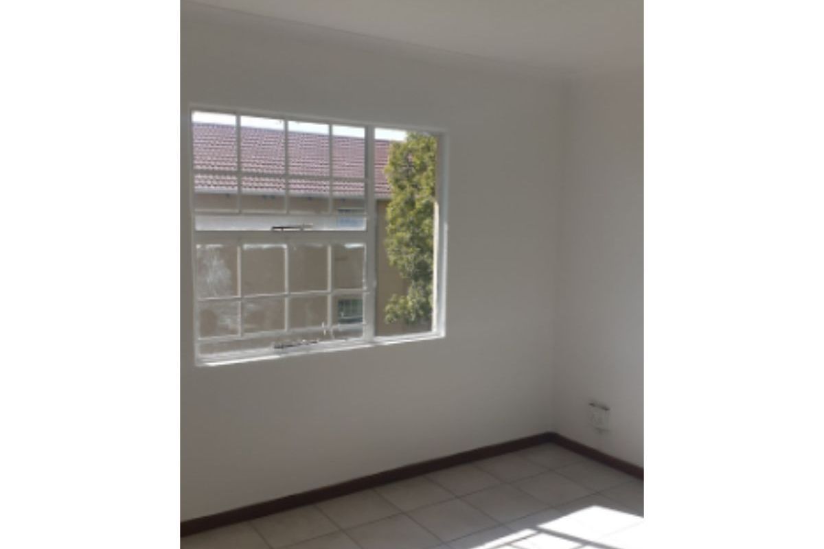 A bright, empty bedroom featuring neutral tiled flooring, white walls, and a grid-pattern window providing natural light.
