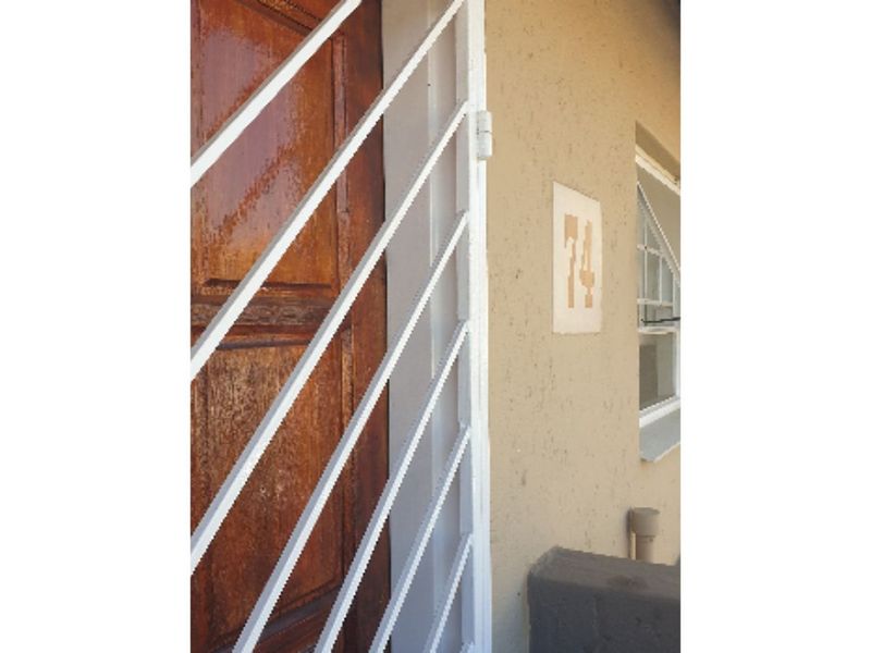 Front entrance of the townhouse featuring a timber door with a white security gate and a visible house number plaque.