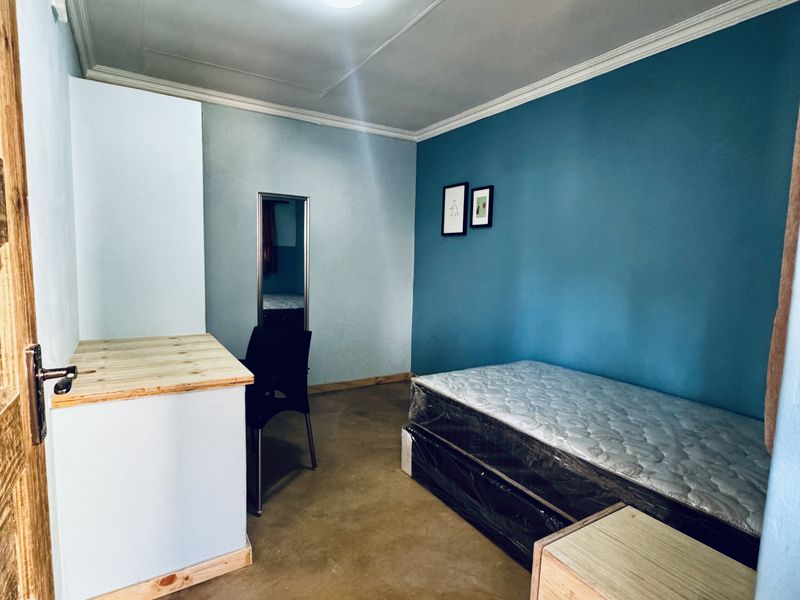 A bedroom featuring a built-in desk and cupboard, with a blue accent wall and concrete flooring.